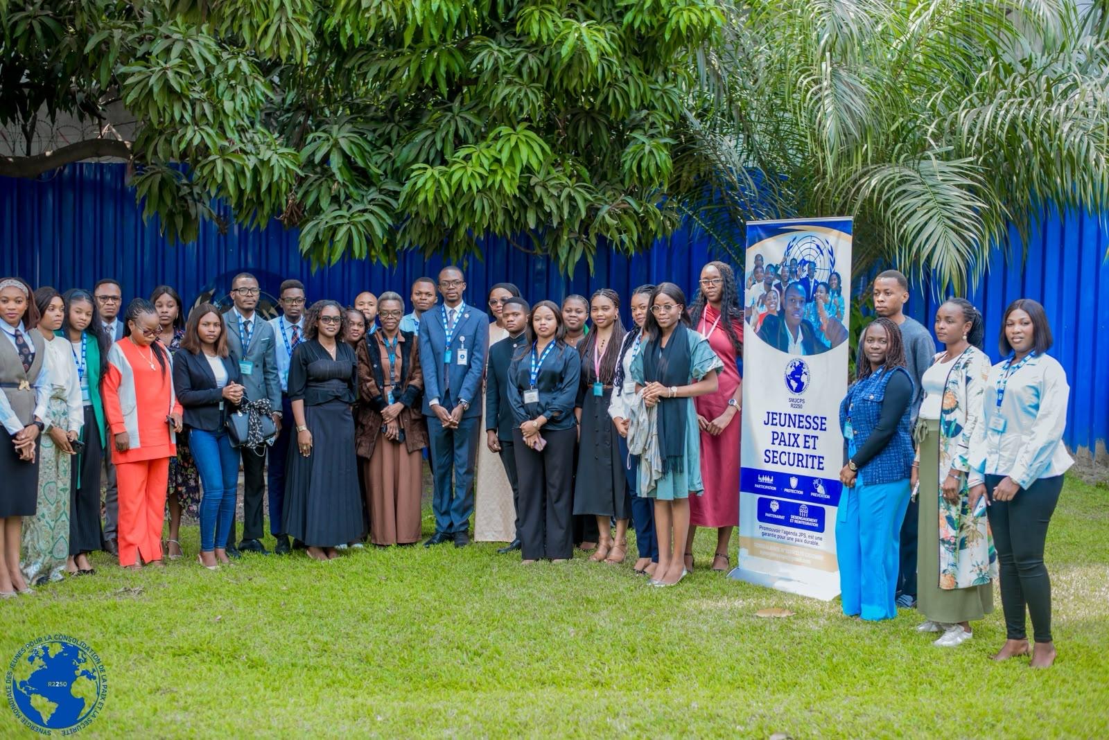 Jeunes leaders réunis dans les jardins du PNUD à Kinshasa lors de la Masterclass diplomatique, devant la bannière Jeunesse Paix et Sécurité